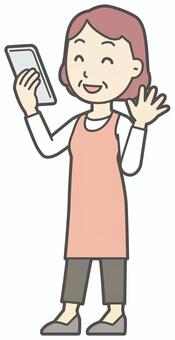  スマホに向かって手を振っているおばさん スマホ,女性,人,主婦,中年,シニア,エプロン,ママ,お母さん,おかんのイラスト素材
